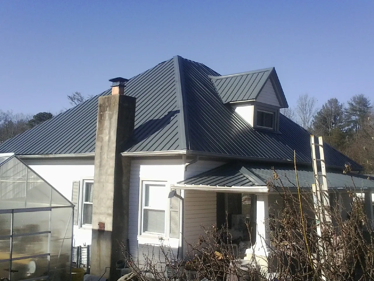 Dark blue standing seam metal roof on a white farmhouse with dormer — Slate & Tile Roof Repair by Roofing Brothers in Ranger