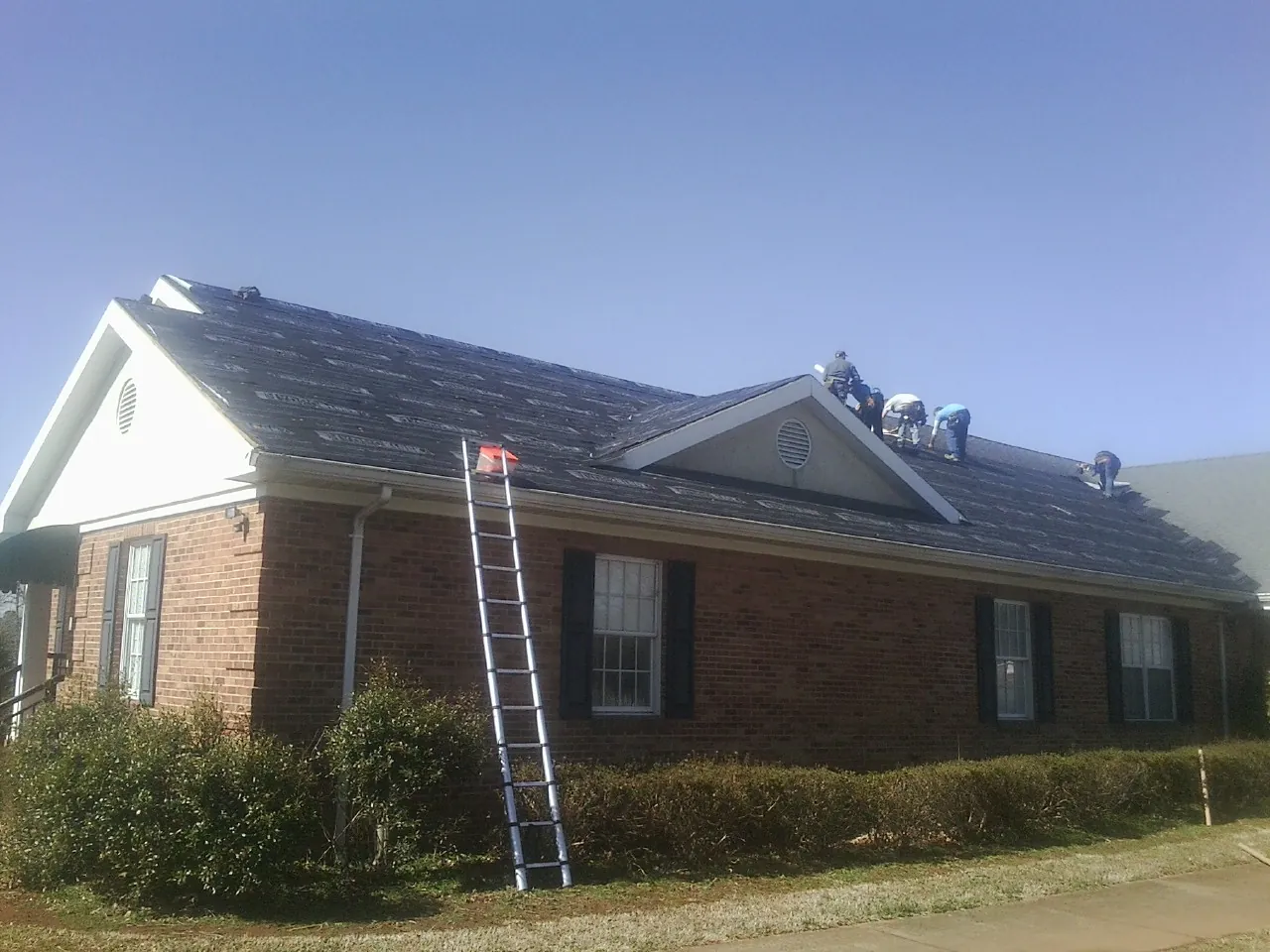 Crew tearing shingles off a brick ranch roof with a ladder set — Emergency Roof Repair work by our crew in Ranger