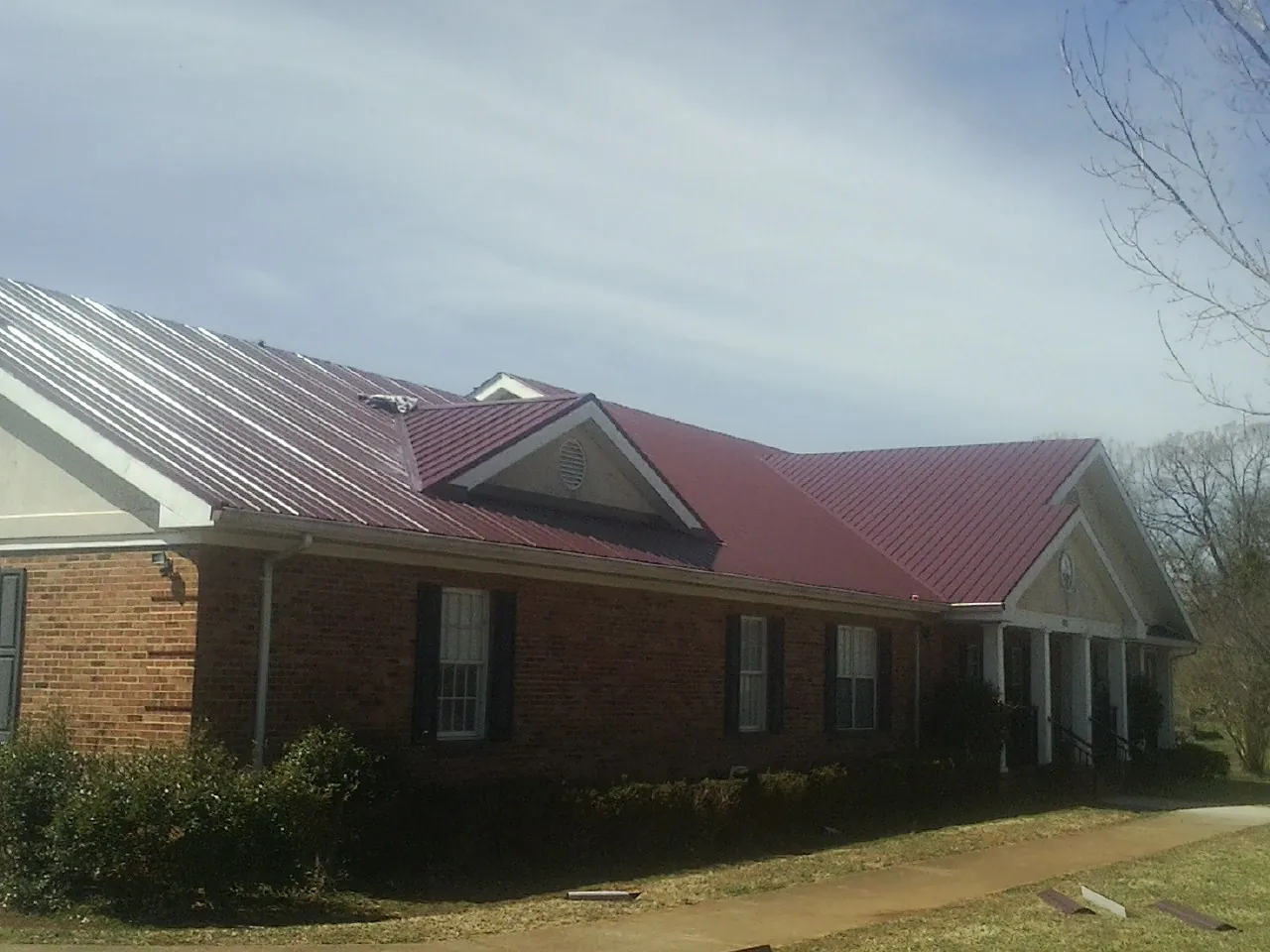 Red metal roof with gabled entries on a long brick building, from a Hail Damage Roof Repair job in Ranger