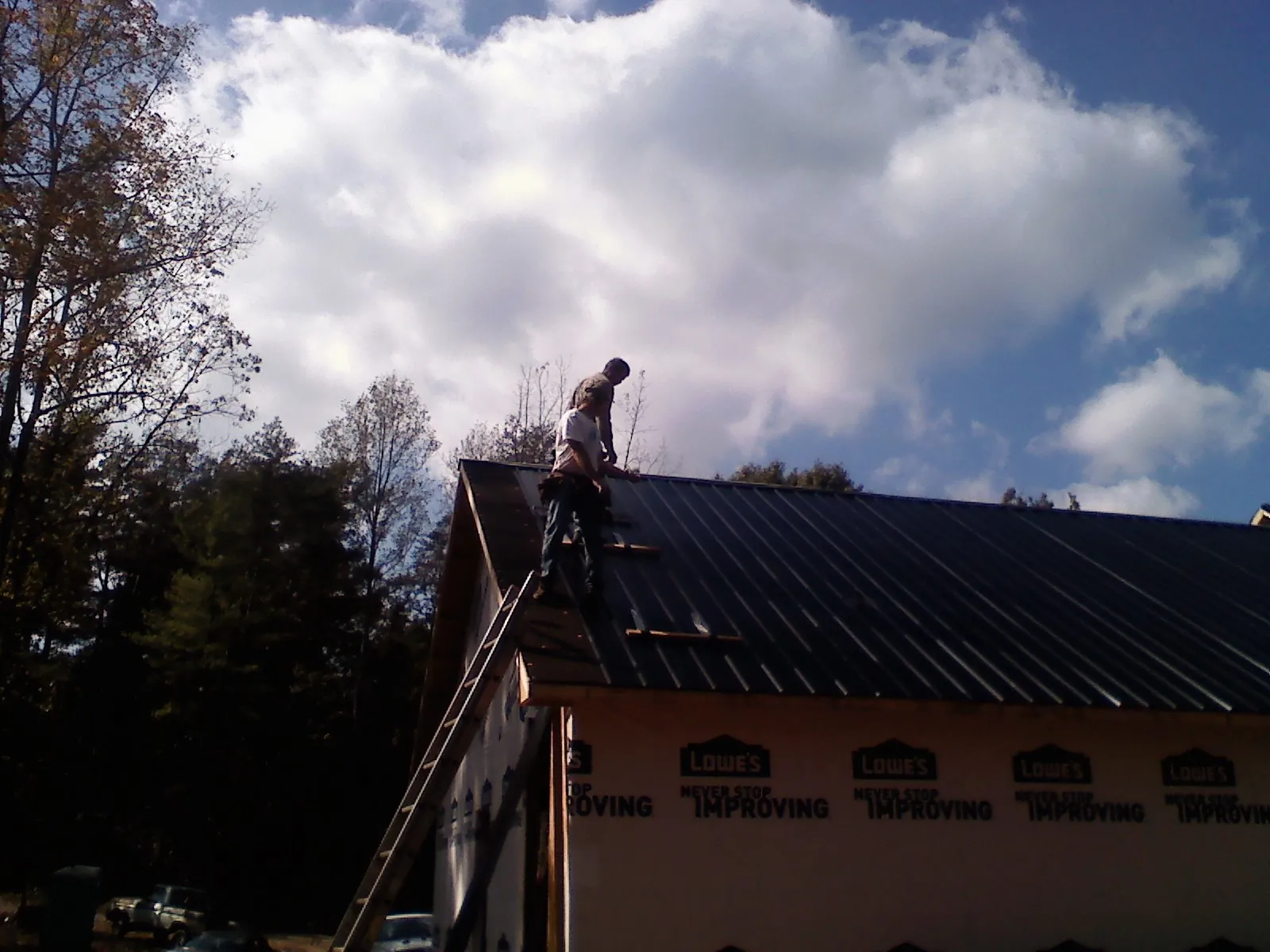 Roofer fastening dark metal panels high against a cloudy sky, from a Roof Inspection job in Ranger